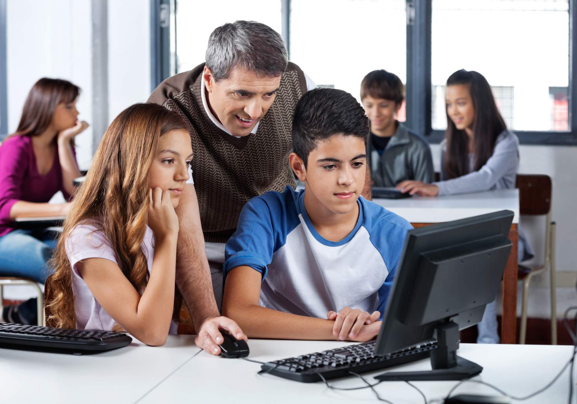 Teacher standing over kids in front of computer screen
